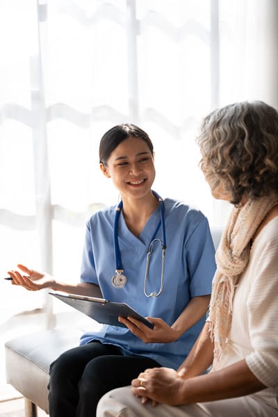 A nurse with a notepad supporting an older patient in a waiting room